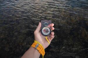 First person view of a man's hand holding a compass against a beautiful seascape. Navigation concept of finding your own way and orientation to the cardinal points photo