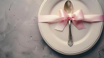 A white plate with a pink ribbon and a silver spoon photo