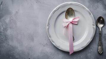 A silver spoon and fork on a white plate with a pink ribbon photo