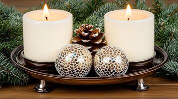 Two candles sit on a table with pine cones and evergreen branches photo