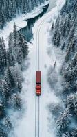 An aerial view of a red train traveling through a snowy forest photo