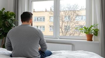 A man sitting on a bed looking out a window photo