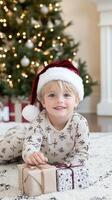 A young boy in pajamas with presents in front of a christmas tree photo
