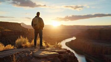 Man standing on edge of cliff overlooking river at sunset photo