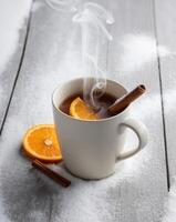 A cup of hot tea with cinnamon sticks and oranges on a snowy table photo