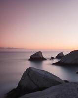 A long exposure photograph of rocks on the shore at sunset photo