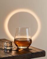 Glass of whisky with ice cubes sitting on wooden table in warm light photo