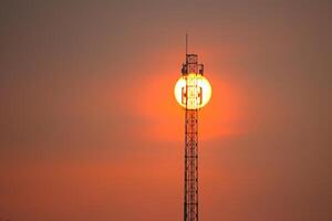 A cell tower with the sun setting behind it photo