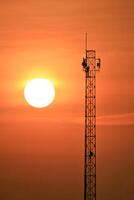 A cell tower with the sun setting behind it photo
