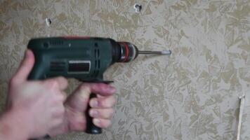 Man drills hole in marbled painted plaster wall. Male hands hold electric drill to make hole with twist drill bit rotating. DIY home improvement video