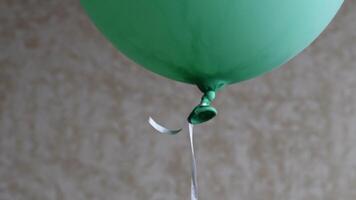 Soft focus to bottom part of green balloon with rubber tail tied with long string on blurred background. Matte green color helium balloon rise up and floating in air video