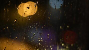Drops of night rain on dirty glass window with golden purple bokeh lights of city traffic. Rainy weather urban background. Cinematic shot with shallow depth of field. Intentional motion blur video