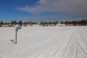 Signpost on frozen lake and the town Norsjo in Sweden. The signpost is pointing to Hamming, Kalvtrask, Vindelalven, Siksele and Norsjo photo