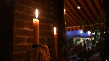 Blurry candle stick flaming in darkness on windowsill with blurry silhouettes behind window. Cozy still life on window in evening. Artistic noise night shooting video