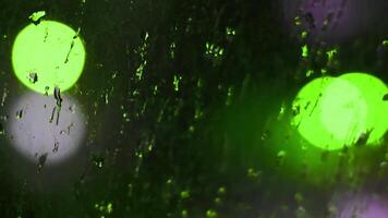 Drops of night rain on dirty glass window with green bokeh lights of city traffic. Rainy weather urban background. Cinematic shot with shallow depth of field. Intentional motion blur blinking lights video