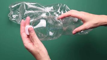 POV female hands crumple and crush transparent plastic bottle for recycling. Crumpled used bottles on green background. First point view preparation of recycled household trash as zero waste video