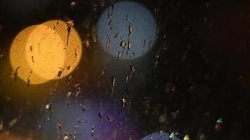 Defocus drops of night rain on dirty glass window with bokeh lights background of city traffic. Bad pour weather urban abstraction. Cinematic shot with shallow depth of field. Intentional motion blur video