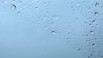 Blurry raindrops on window glass surface closeup. Closeup shot of water drops on car windshield. Shades of light blue background with copy space video