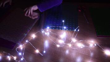 Blurred foreground of defocus Christmas string lights and toddler hands shift glittering craft papers on background. Holiday or kids birthday craft projects video