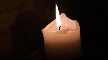 Single melted wax candle burning with dark background and copy space. Paraffin candle flame in darkness. Background of remembrance or Halloween celebration video