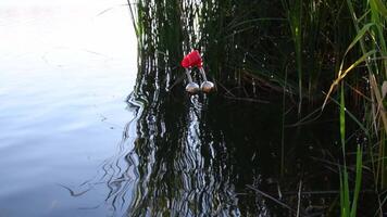 Closeup of small metal jingle bells hanging on red clothespin at fishing line and shaking in wind. Tranquil lake water surface with copy space. Equipment for fishing sport and hobby video