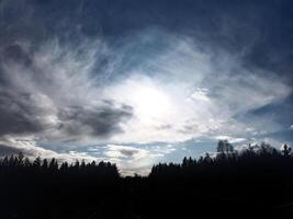 Sun and clouds over a forest silhouette photo