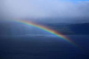 Dark shot of a rainbow in front of mountain lake photo