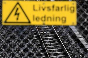 Defocused fence and warning sign in front of rail track. The sign says Lifsfarlig ledning - Cable dangerous to life - in Swedish photo