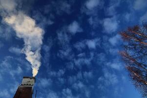 Old chimney on a house emitting white smoke in a sky with fluffy clouds photo