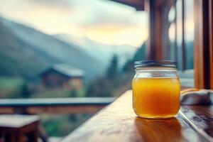 A jar of orange juice sits on a table in front of a mountain view photo