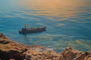 A toy boat floating in the water near rocks photo