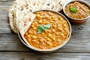 A bowl of curry and two tortillas on a wooden table photo