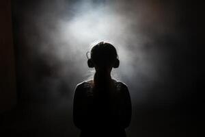 A silhouette of a girl with headphones on in a dark room photo