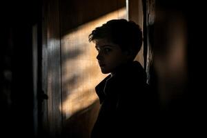 A boy stands in the shadows of a doorway photo