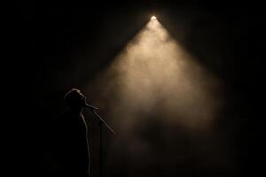 Silhouette of a man singing in front of a spotlight photo