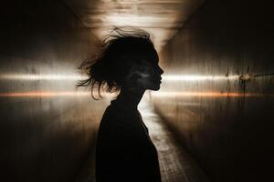 A woman is standing in a dark tunnel with light coming from the ceiling photo