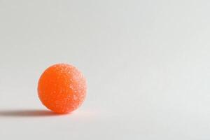 A single orange sugared candy rests on white photo