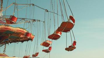 Red chairs on a chain swing ride against a blue sky. photo