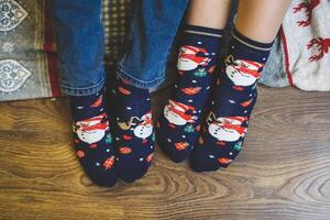Couple relax. Two pair of feet in colorful ornamented Christmas socks over blurred Xmas room background, selective focus photo
