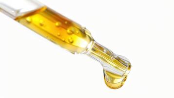 A Golden Drop of Liquid Dripping From a Glass Dropper Against a White Background photo