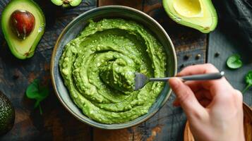 A Hand Reaches for a Forkful of Creamy Avocado Dip on a Rustic Wooden Table photo