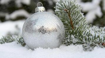 A Silver Christmas Ornament Rests in the Snow Near a Pine Branch photo