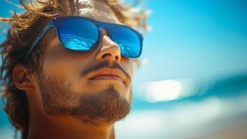 Young man in sunglasses enjoys beach day. A young man relaxes on the beach under the sun, wearing sunglasses and enjoying a peaceful moment by the ocean. photo