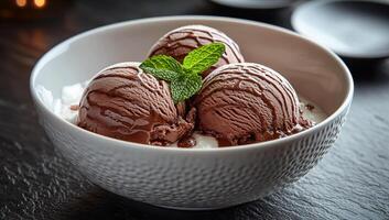 Chocolate ice cream served in a decorative bowl. Three scoops of rich chocolate ice cream, topped with a mint leaf, create an inviting dessert. photo