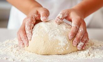 A person is kneading dough on a table. The dough is covered in flour and the person's hands are covered in it photo