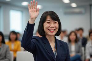 Photograph of an Asian woman with short black hair, wearing a grey blazer and white shirt, enthusiastically raising her hand in a classroom setting. photo