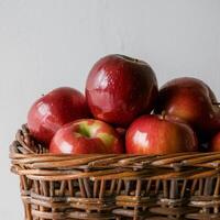 Wicker basket filled with glossy red apples, contrasting against plain white background For Social Media Post Size photo