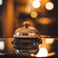 Shiny metallic bell with golden top on reflective surface, warm golden hue background For Social Media Post Size photo