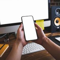 Hands with smartphone in front of off monitor, yellow keyboard, speaker, notebook visible For Social Media Post Size photo