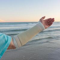 Forearm in cast with serene beach and gentle ocean waves in the background For Social Media Post Size photo